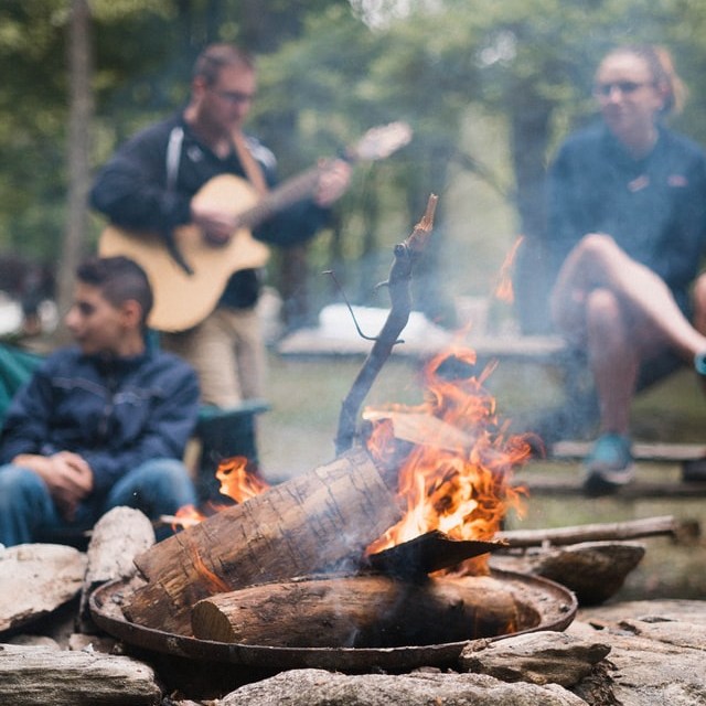 People around the campfire with a person playing guitar